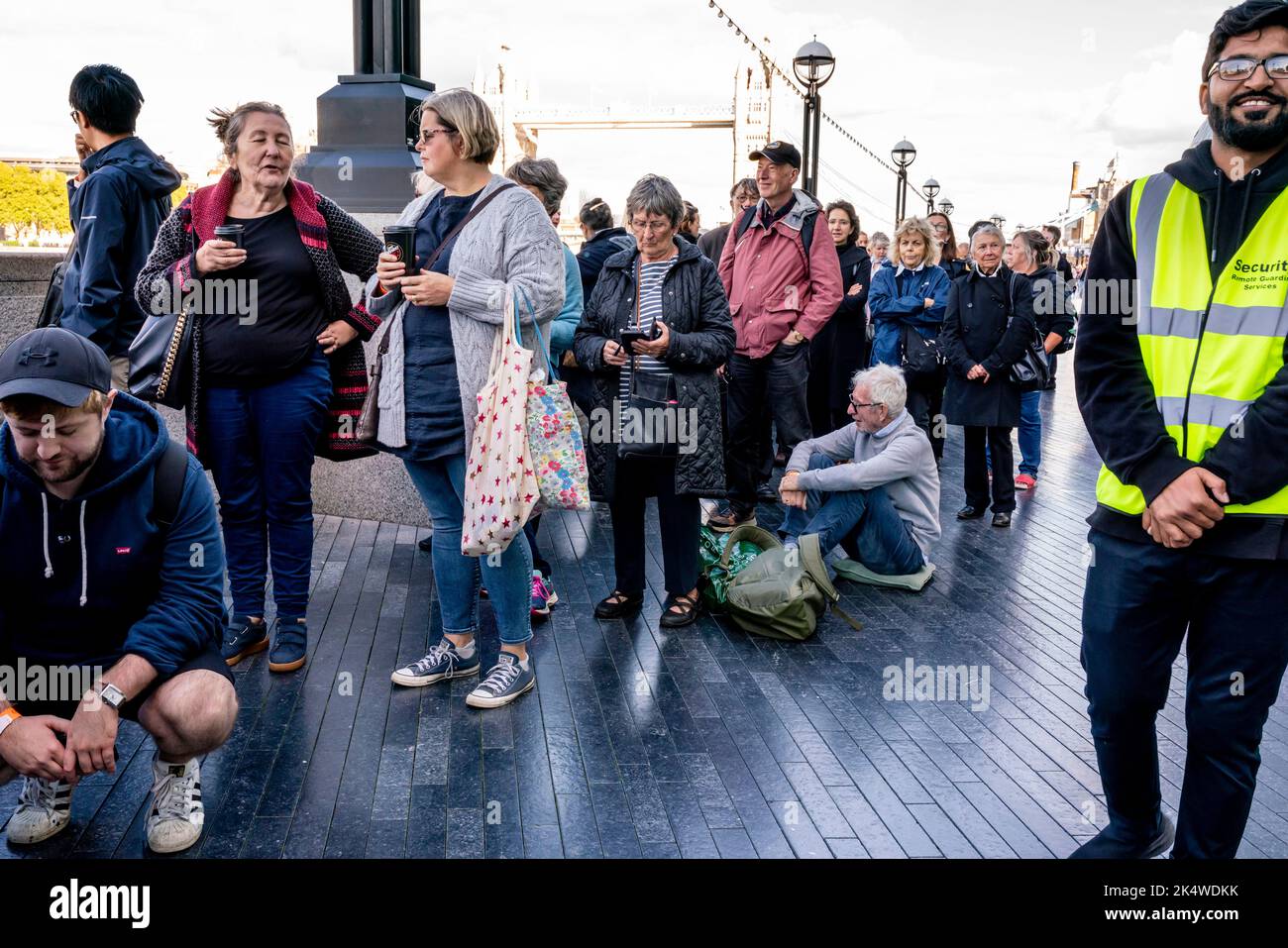 Müde Menschen setzen sich hin und ruhen sich aus, während sie in der Warteschlange stehen, um die Königin in der Westminster Hall, London, Großbritannien, liegen zu sehen. Stockfoto
