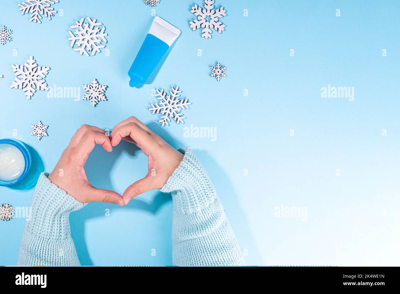 Frau, die Wintercreme für die Hände verwendet. Mädchen Hände mit Creme flach lag auf hellblauem Hintergrund mit künstlichen Schneeflocken und verschiedenen Handcremes. Winte Stockfoto