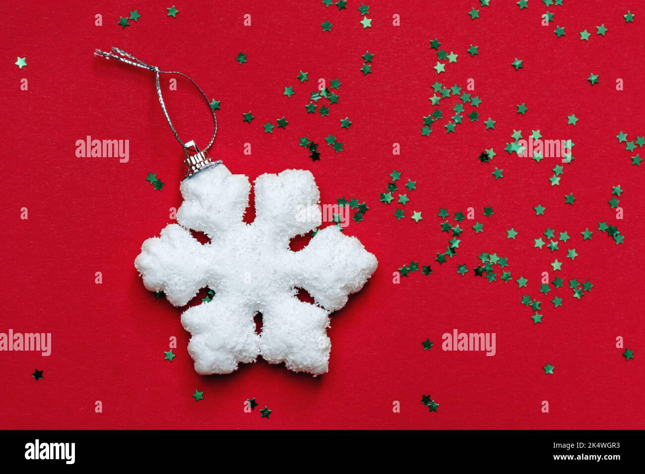 Weiße große Schneeflocke und kleine grüne funkelnde dekorative glänzende Sterne leuchten auf roter Oberfläche. Blick von oben. Konzept für Weihnachten und Neujahr Stockfoto