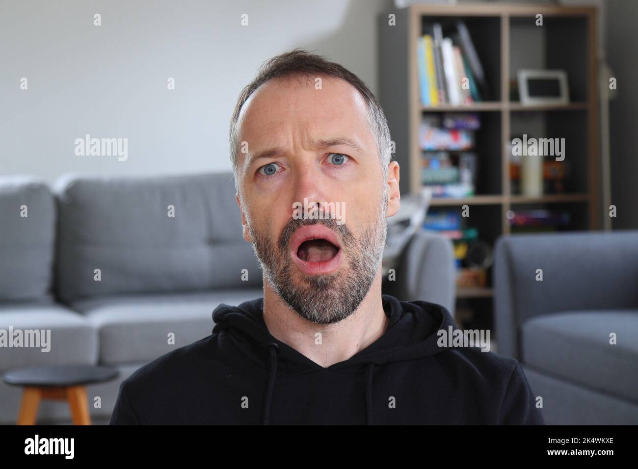 Der Mensch schockiert und ungläubiger Ausdruck. Bärtiger Mann mit lässigem schwarzem Hoodie. Erwachsener kaukasischer Mann im Jahr 30s oder 40s schockiert. Stockfoto