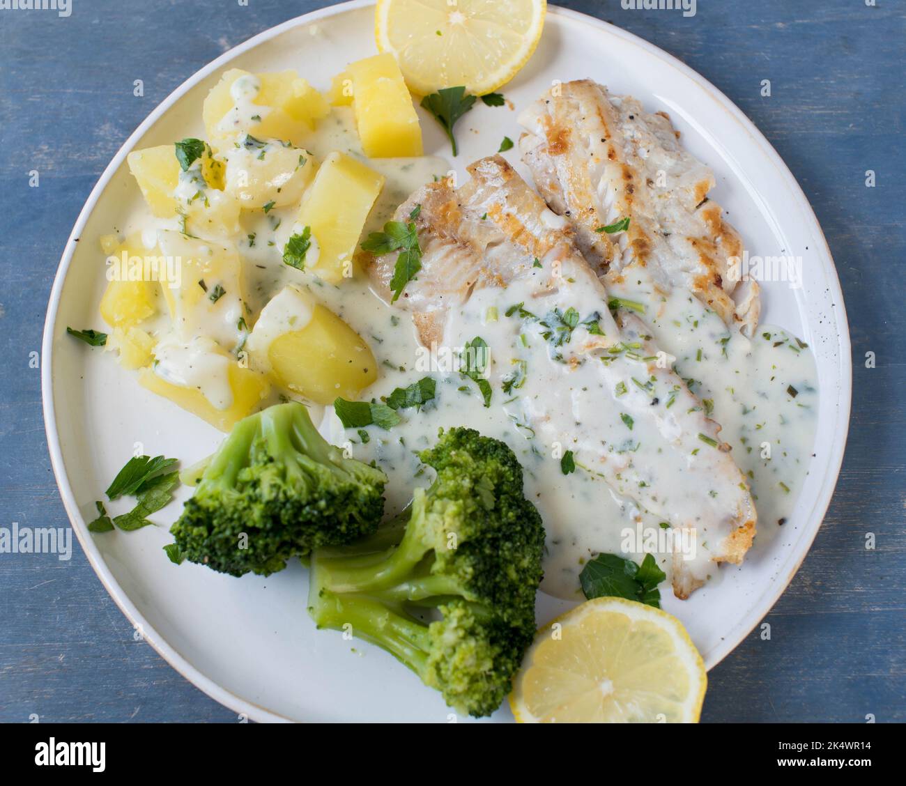 Gebratenes natürliches Fischfilet mit Brokkoli, Boildkartoffeln und Kräutern, Bechamelsauce auf einem Teller Stockfoto