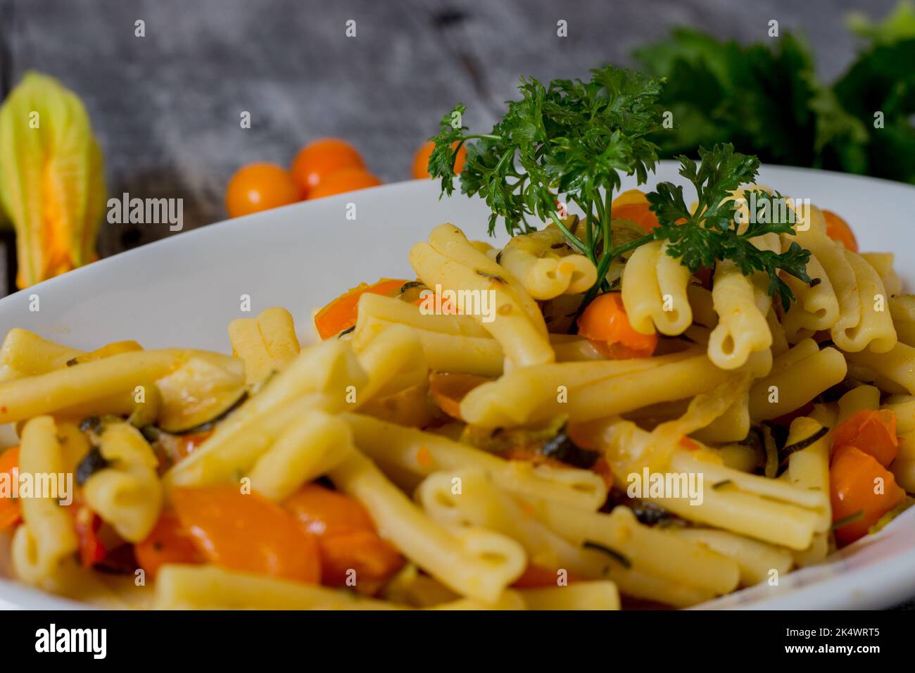 Pasta mit Zucchini, Zucchiniblüten, gelben Datterini-Tomaten auf einem weißen Teller serviert. Vegetarisches Rezept Stockfoto