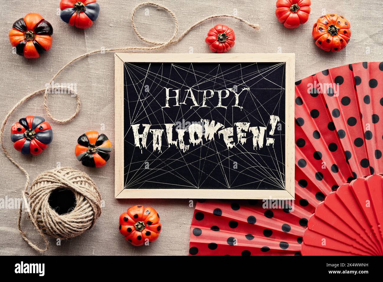 Text Frohes Halloween mit Spinnweben auf Kreidetafel. Herbstliche Einrichtung um eine Tafel. Orange Mini Kürbisse schwarz lackiert und Fächer mit Tupfen auf beige Stockfoto