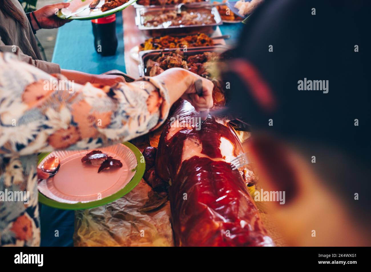 Die Hände unwiedererkennbarer Menschen drängen sich herum und bekommen ein Stück des beliebten und köstlichen gerösteten ganzen Schweines oder „Lechon Baboy“ auf dem Buffettisch Stockfoto