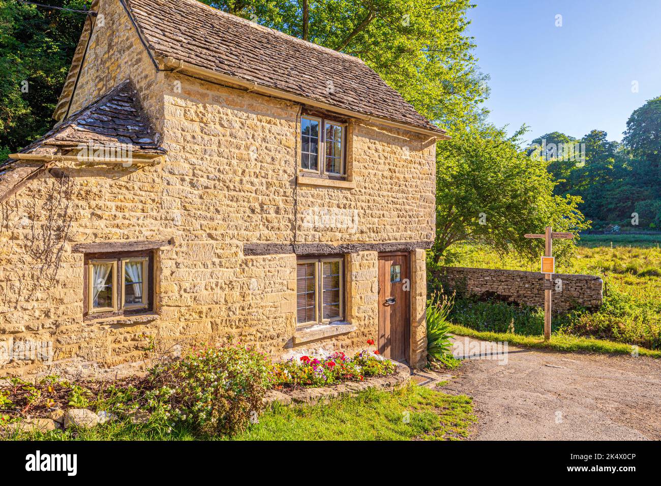 Im Hochsommer ist es am frühen Morgen hell auf einem typischen Steinhäuschen im Cotswold-Dorf Bibury, Gloucestershire, England Stockfoto