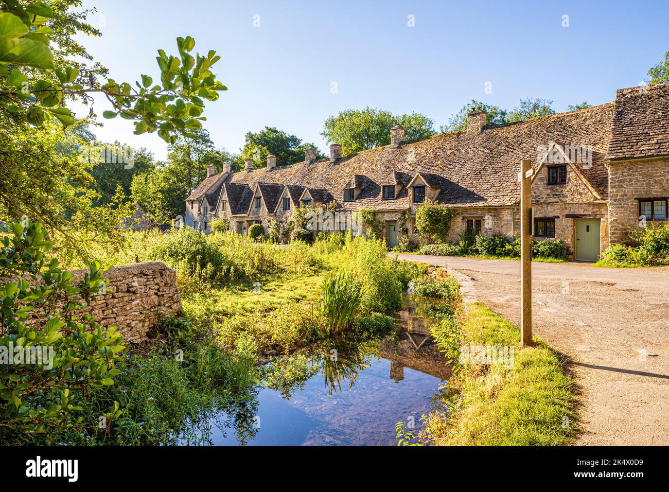 Im Hochsommerlicht am frühen Morgen in der Arlington Row im Cotswold-Dorf Bibury, Gloucestershire, England Stockfoto