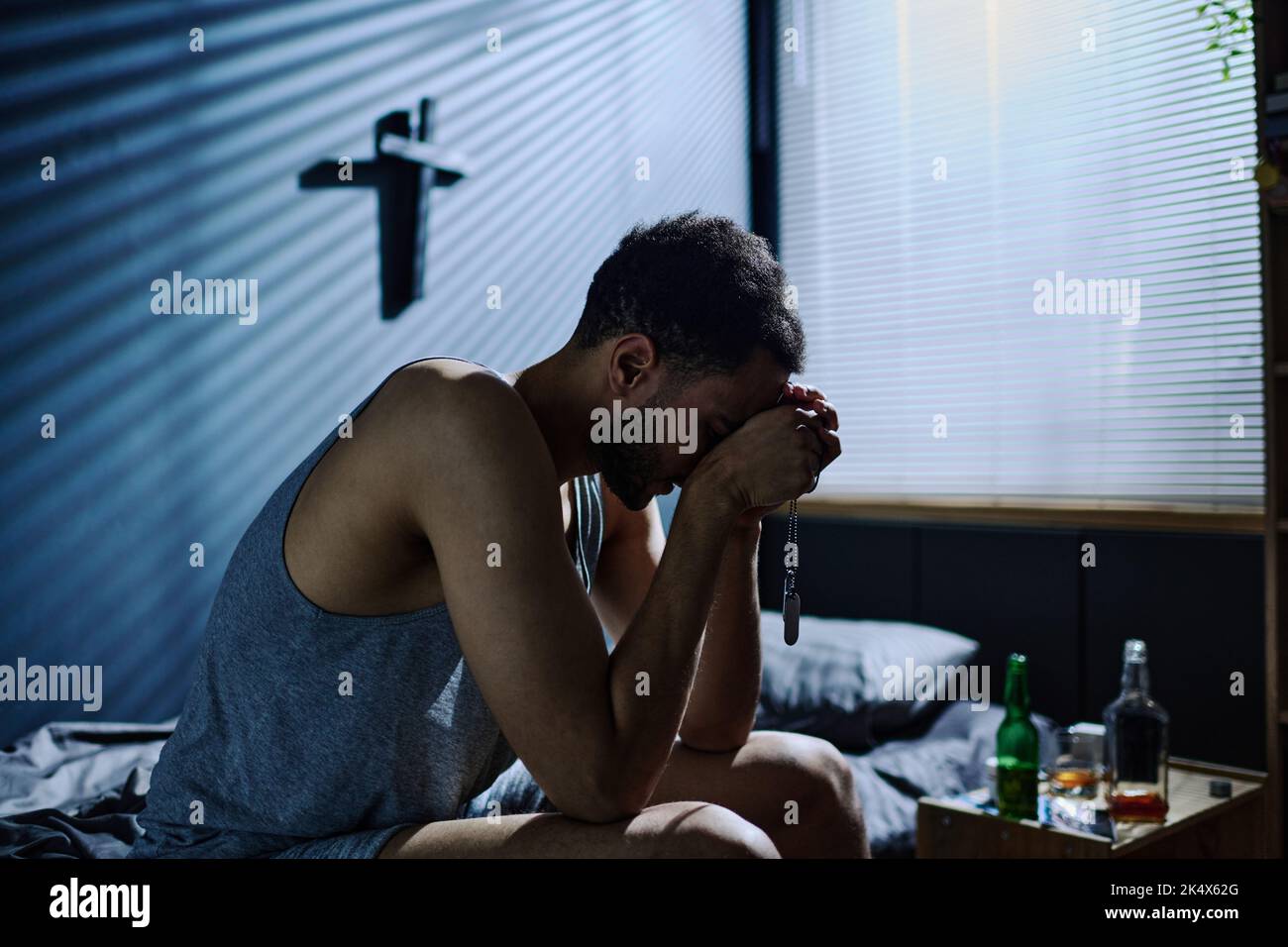 Seitenansicht eines jungen, untröstlichen Mannes mit posttraumatischem Syndrom, der sich nach vorne beugte, während er mit Händen an Gesicht auf dem Bett saß Stockfoto