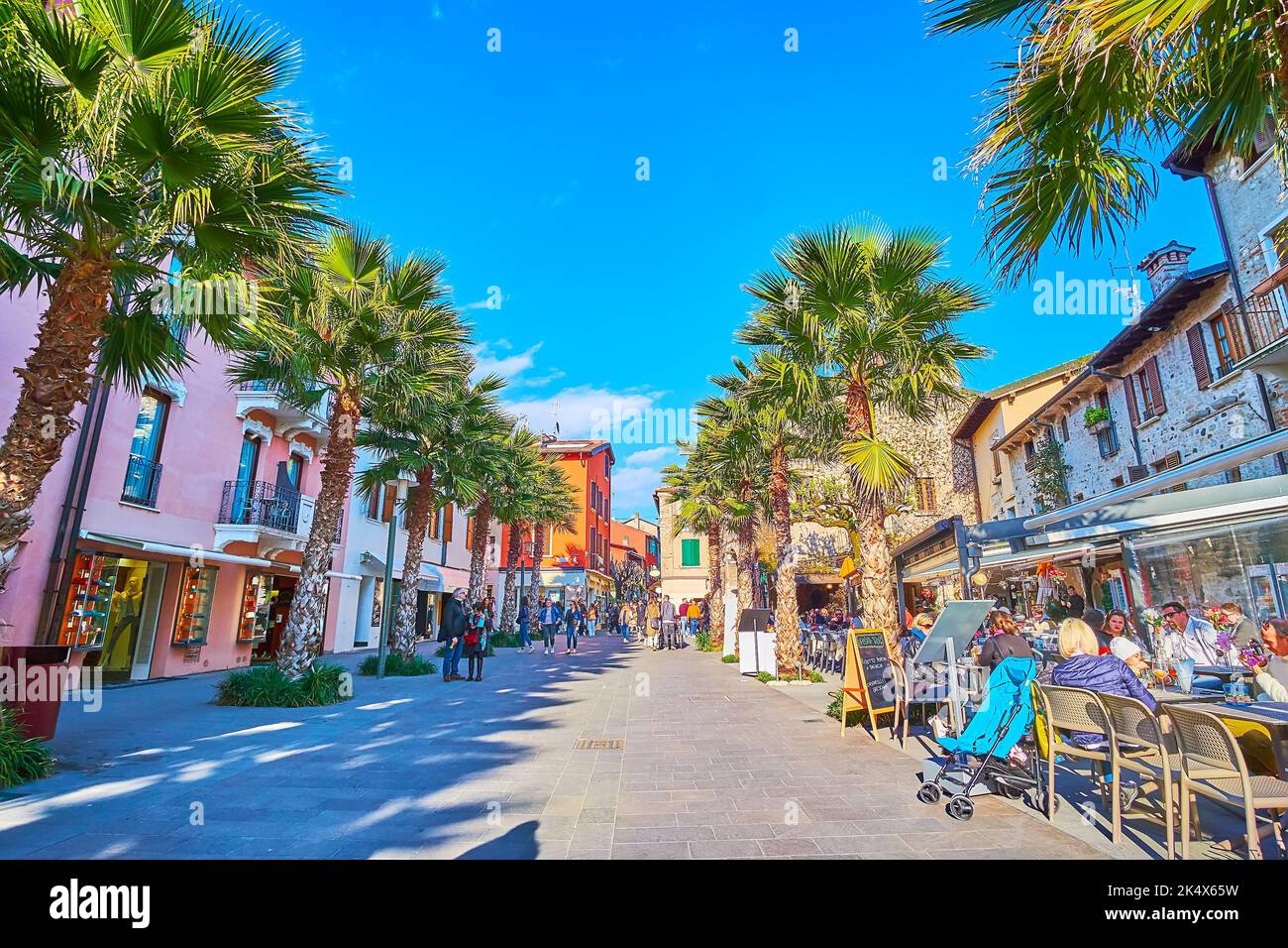 SIRMIONE, ITALIEN - 10. APRIL 2022: Die malerische Piazza Flaminia mit bunten Häusern, Restaurants, Cafés und hohen Palmen, die den Schatten spenden, am April Stockfoto