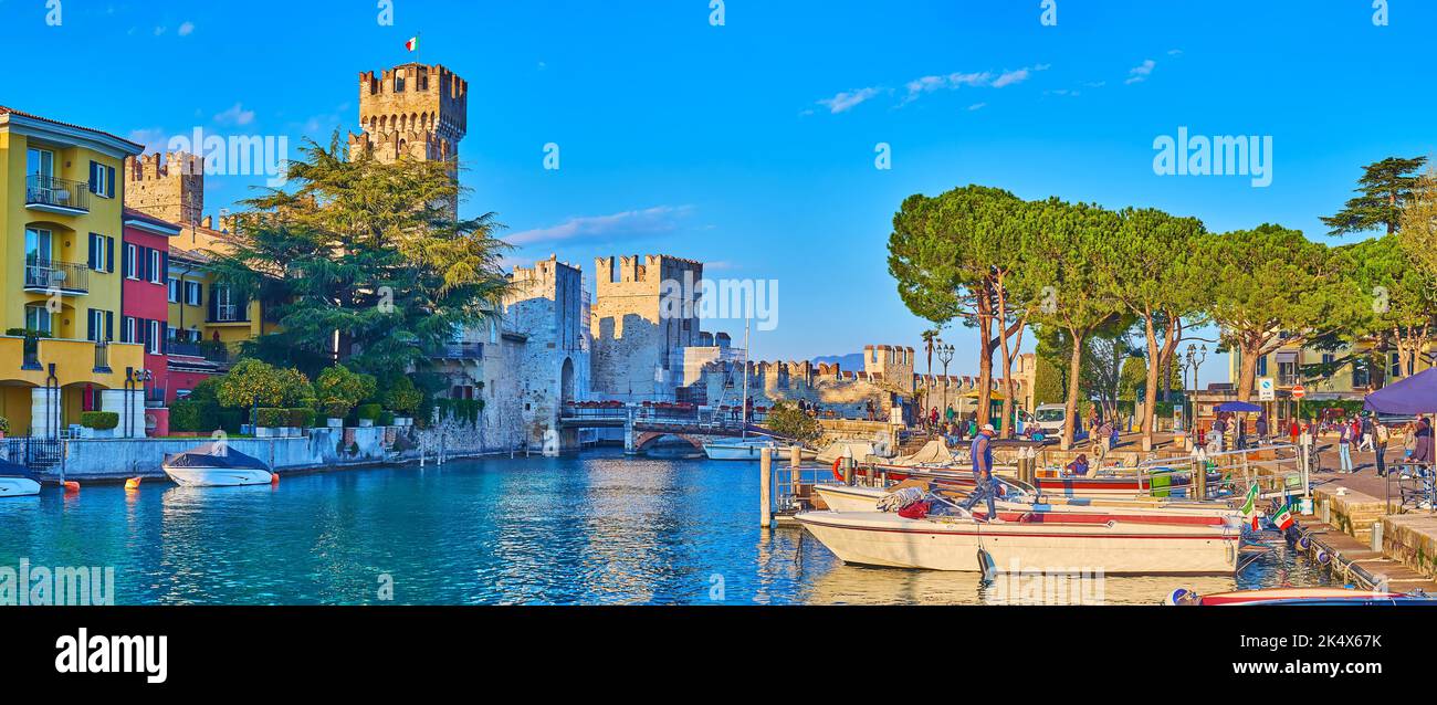 Panorama des kleinen Jachthafens von Sirmione Resort gegen die farbigen Häuser, Hotels, Scaligero Castle und kleine Boote, am Ufer festgemacht, Lombardei, Es Stockfoto