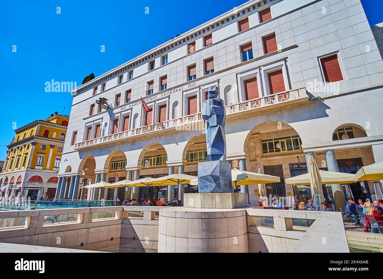 BRESCIA, ITALIEN - 10. APRIL 2022: Die moderne Steinstatue in Fontana del Bigio und Palazzo Assicurazioni Generali im Hintergrund, am 10. April in Stockfoto