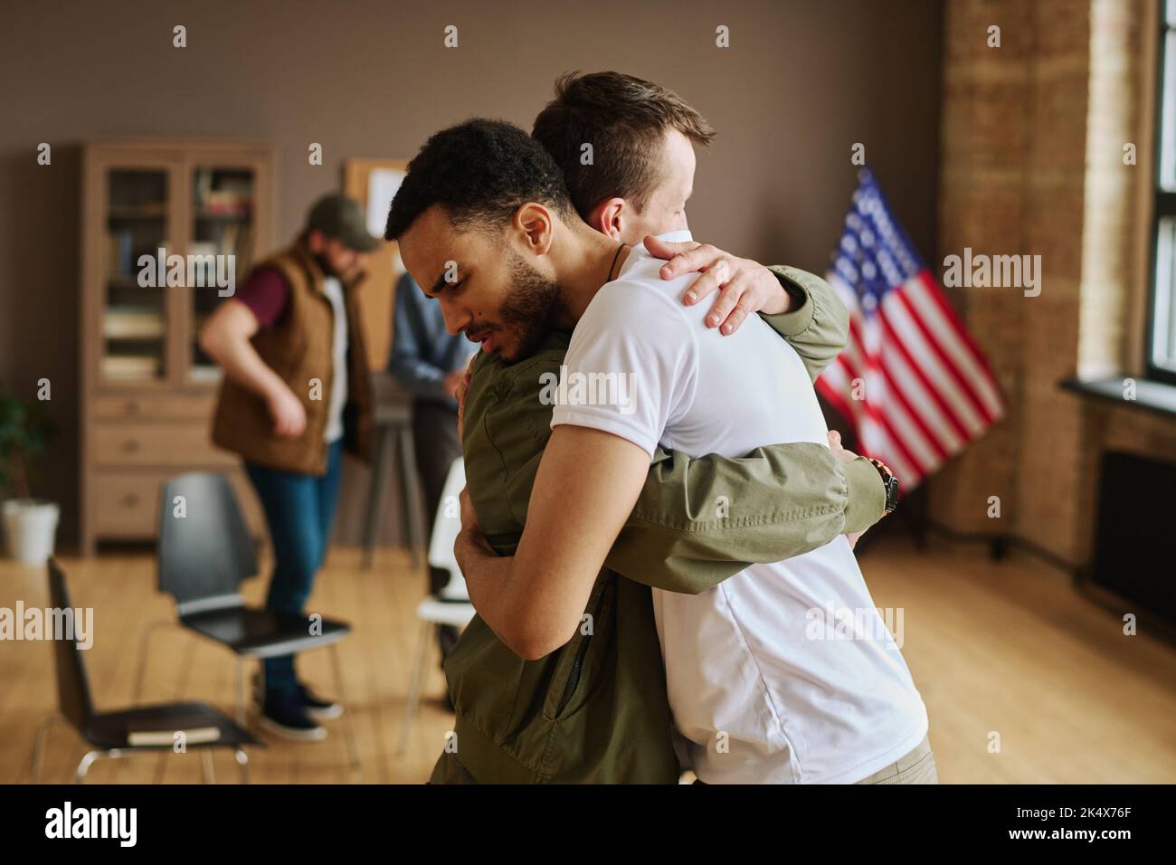 Der junge Mann umarmte seinen Freund mit posttraumatischem Syndrom während einer psychologischen Sitzung, nachdem er Fälle schlechter Lebenserfahrung besprochen hatte Stockfoto