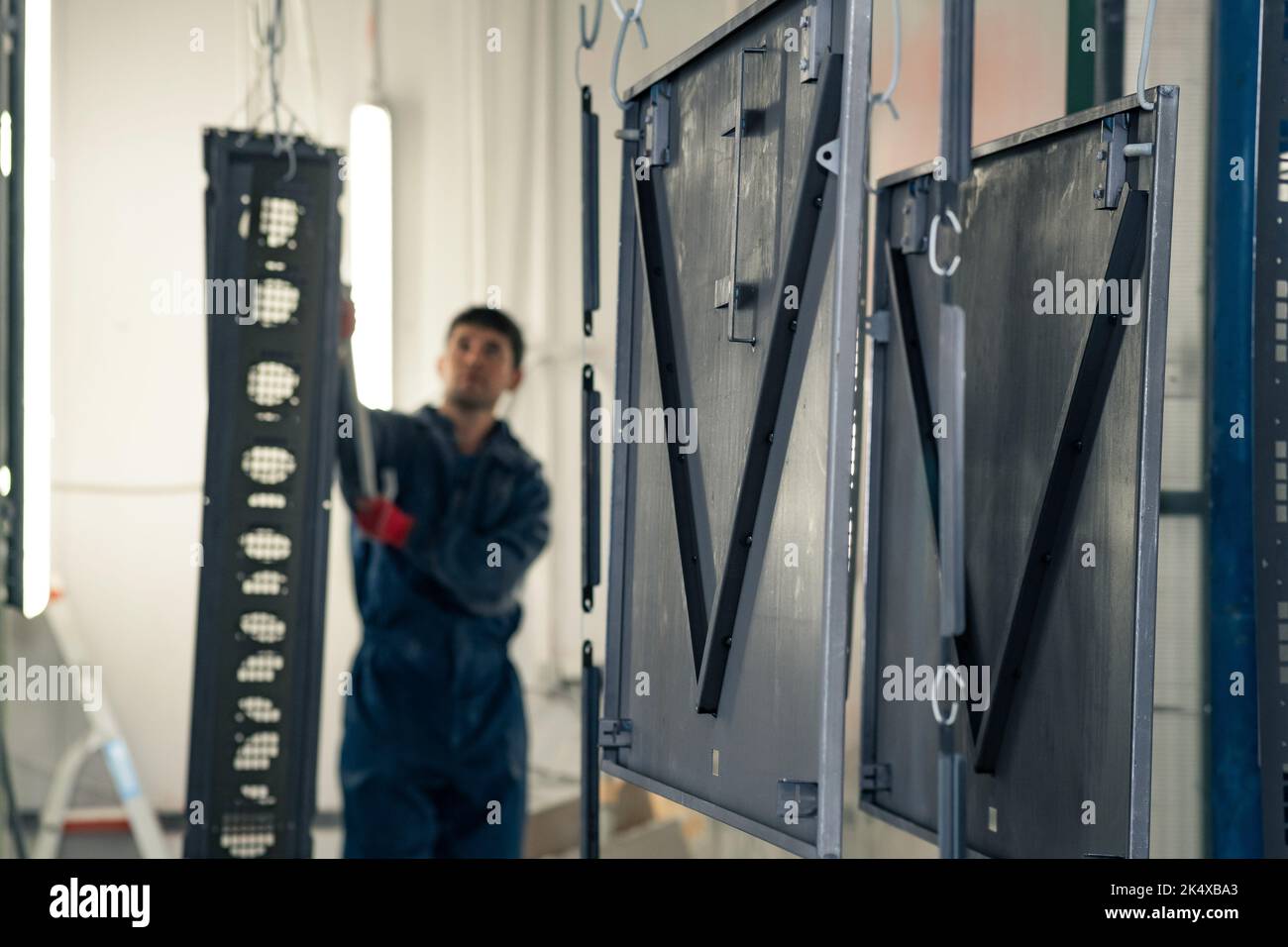 Perm, Russland - 21. September 2022: Arbeiter transportiert Metallteile zu einer Pulverbeschichtungskabine Stockfoto