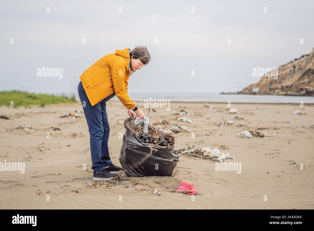 Plastikmüll. Meer- und Meeresverschmutzung. Strand sauber machen. Junger Mann pflückt gebrauchte Plastikflaschen am Sandufer. Sammeln von Umweltaktivisten Stockfoto