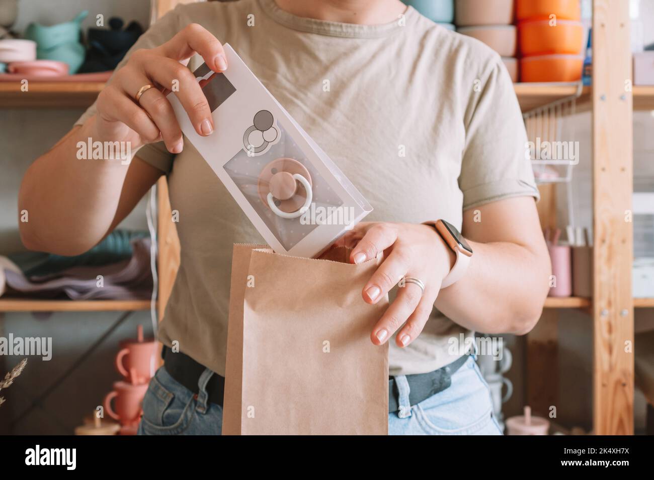 Zugeschnittenes Foto von Geschäftsfrau Hände Verpackung, Vorbereitung Paket für die Lieferung Paket an den Käufer. Frau legt Beruhigungssauger in Kraftpapierbeutel. Kleinunternehmen Stockfoto