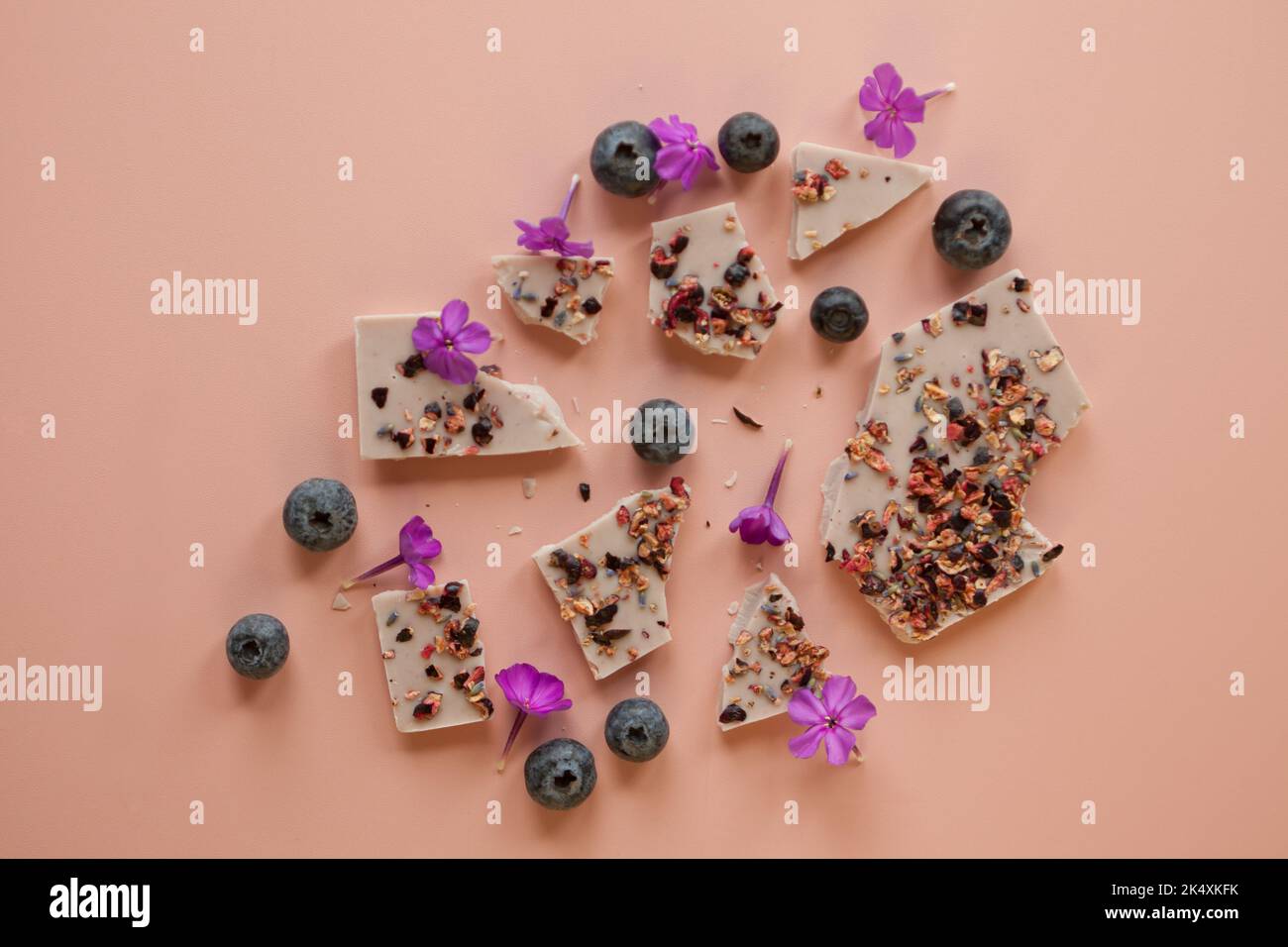 Handgemachte rosa Schokolade mit Beeren und Blumen. Gebrochene Riegel mit Haselnüssen, Mandeln und Himbeeren Stockfoto