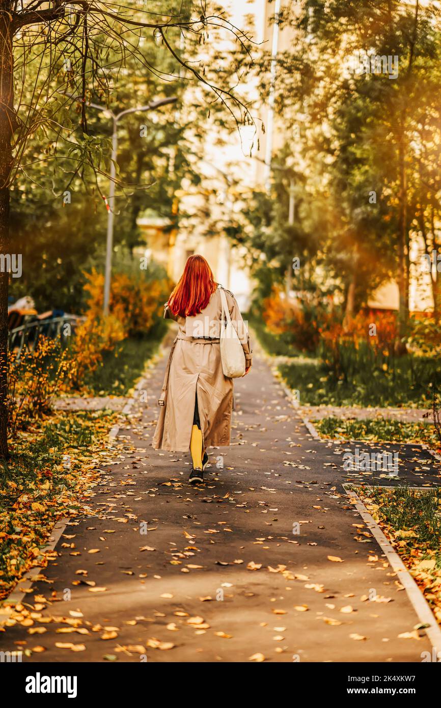 Herbsttag, Spaziergang in der Stadt unter den gefallenen Blättern. Nicht erkennbares rothaariges Mädchen, Rückansicht Stockfoto