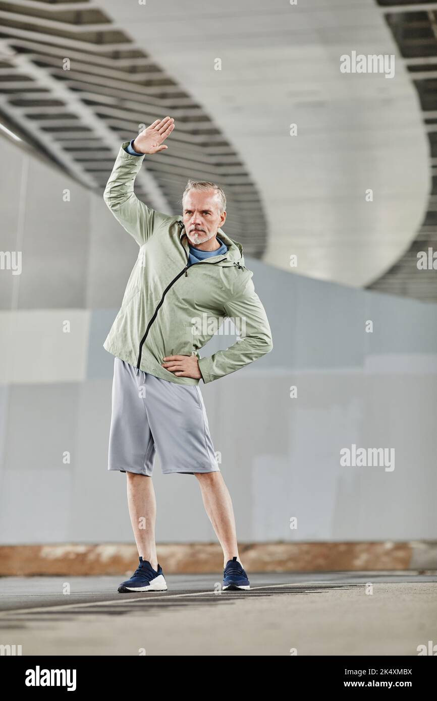 Minimales Porträt eines aktiven, reifen Mannes, der sich während des Outdoor-Trainings in der Stadt dehnt und sich aufwärmt Stockfoto