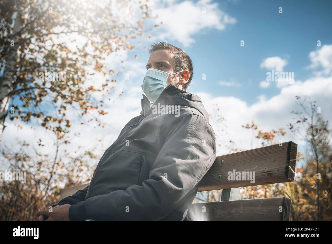 03. Oktober 2022: Junger Mann mit Schutzmaske auf Einer Parkbank im Herbst, Maske zum Schutz vor Corona Virus, Covid 19. Symbolbild Corona Stockfoto