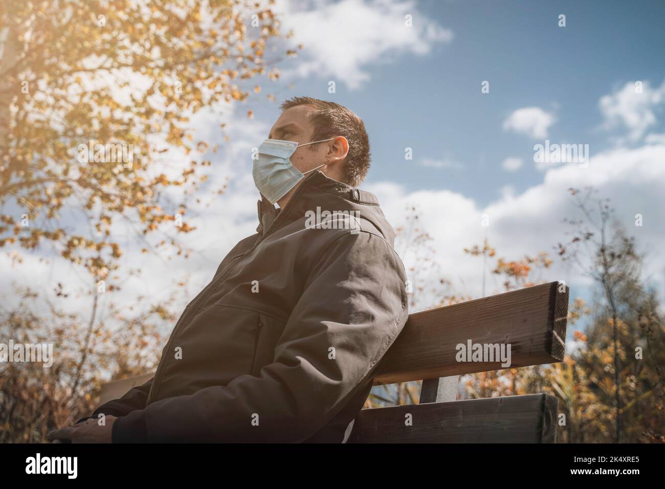 03. Oktober 2022: Junger Mann mit Schutzmaske auf Einer Parkbank im Herbst, Maske zum Schutz vor Corona Virus, Covid 19. Symbolbild Corona Stockfoto