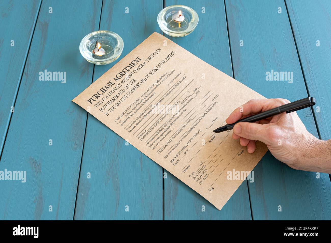 Mann mit Füllfederhalter unterzeichnet Vertrag neben brennenden Kerzen. Stockfoto