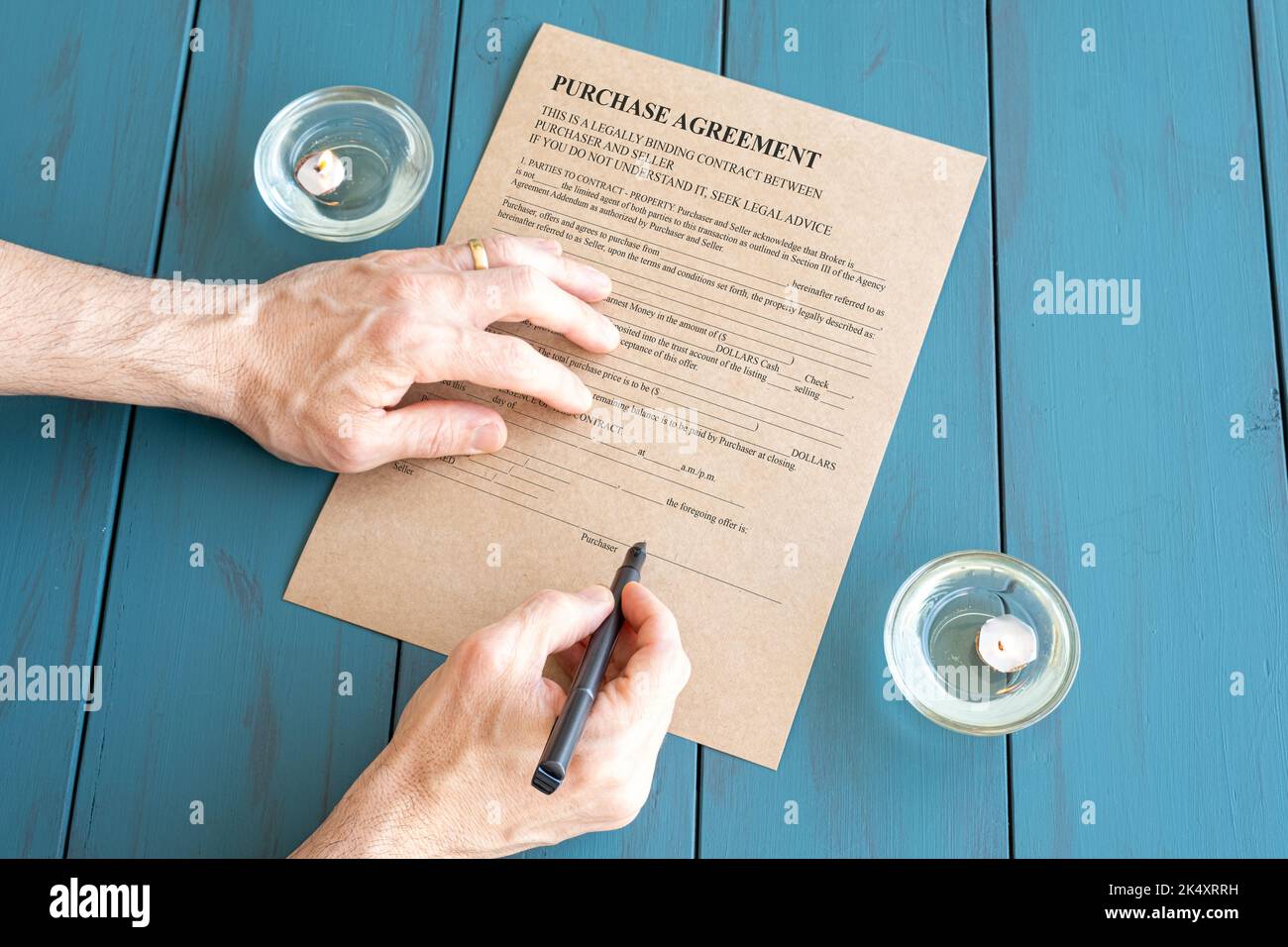 Männerhände mit Füllfederhalter unterzeichnen Vertrag neben brennenden Kerzen. Stockfoto