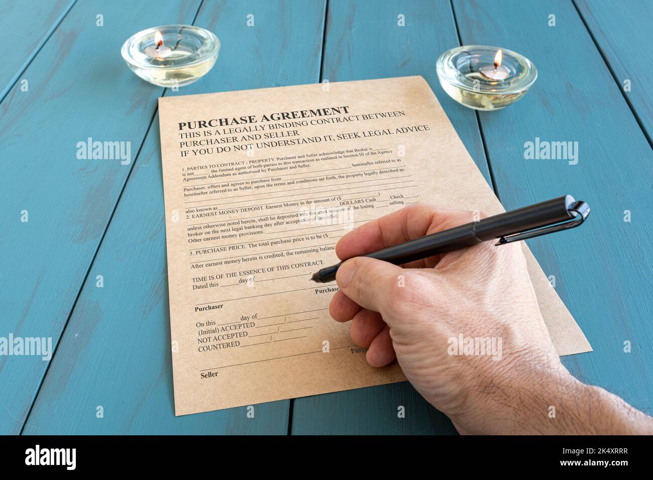 Die Hand des Mannes mit dem Füllfederhalter unterschreibt den Vertrag neben angezündeten Kerzen. Stockfoto