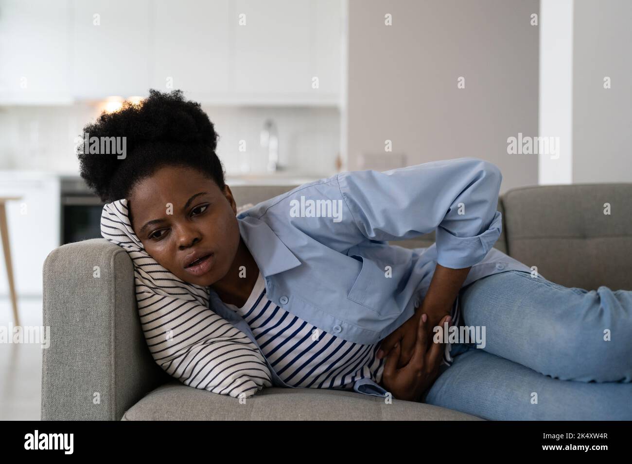 Afroamerikanische Frau mit gesundheitlichen Problemen, die an Krämpfen und Magenschmerzen leidet, liegt auf dem Sofa Stockfoto