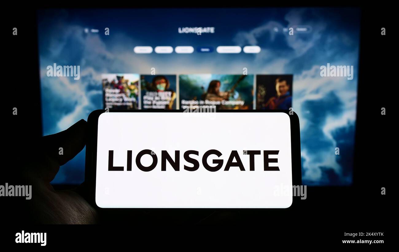 Person mit Mobiltelefon und Logo der Lions Gate Entertainment Corporation (Lionsgate) auf dem Bildschirm vor der Webseite. Konzentrieren Sie sich auf die Telefonanzeige. Stockfoto