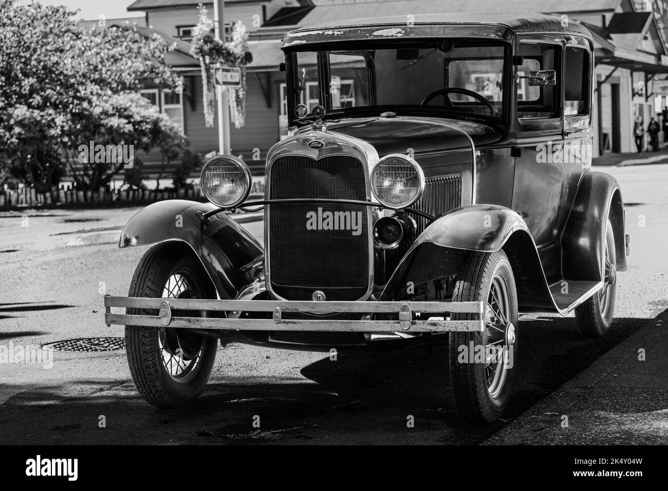 Ein Oldtimer-Ford-Auto, das in einer Straße unter dem hellen Sonnenlicht in Graustufen geparkt wurde Stockfoto