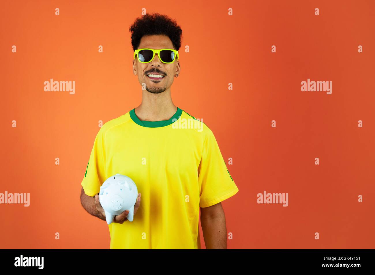 Fußballspieler - Schwarzer Mann feiert Holding Schwein Münze isoliert auf Orange Stockfoto