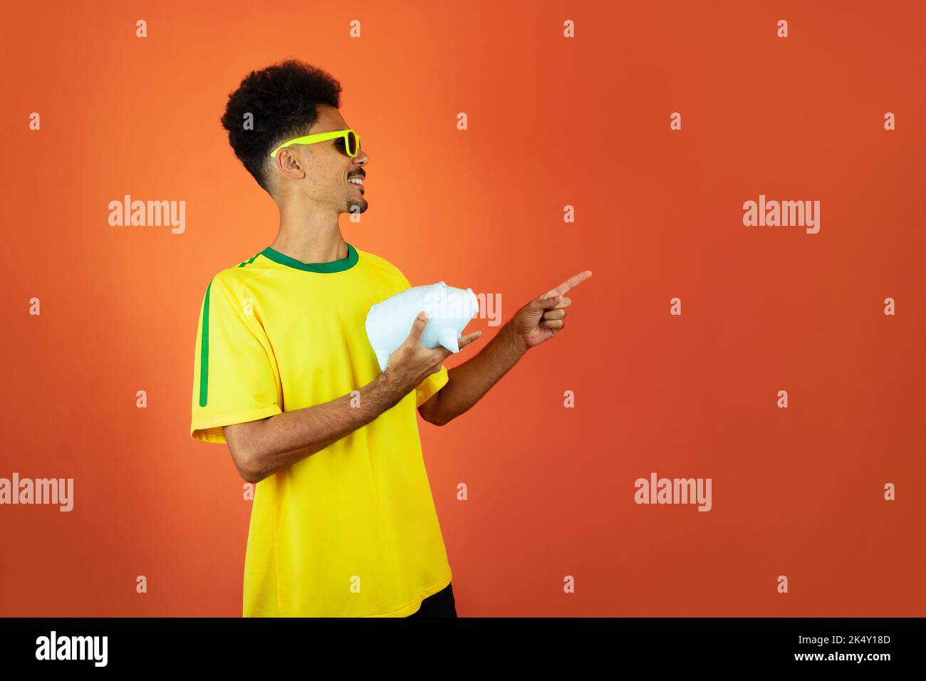 Fußballspieler - Schwarzer Mann feiert Holding Schwein Münze isoliert auf Orange Stockfoto