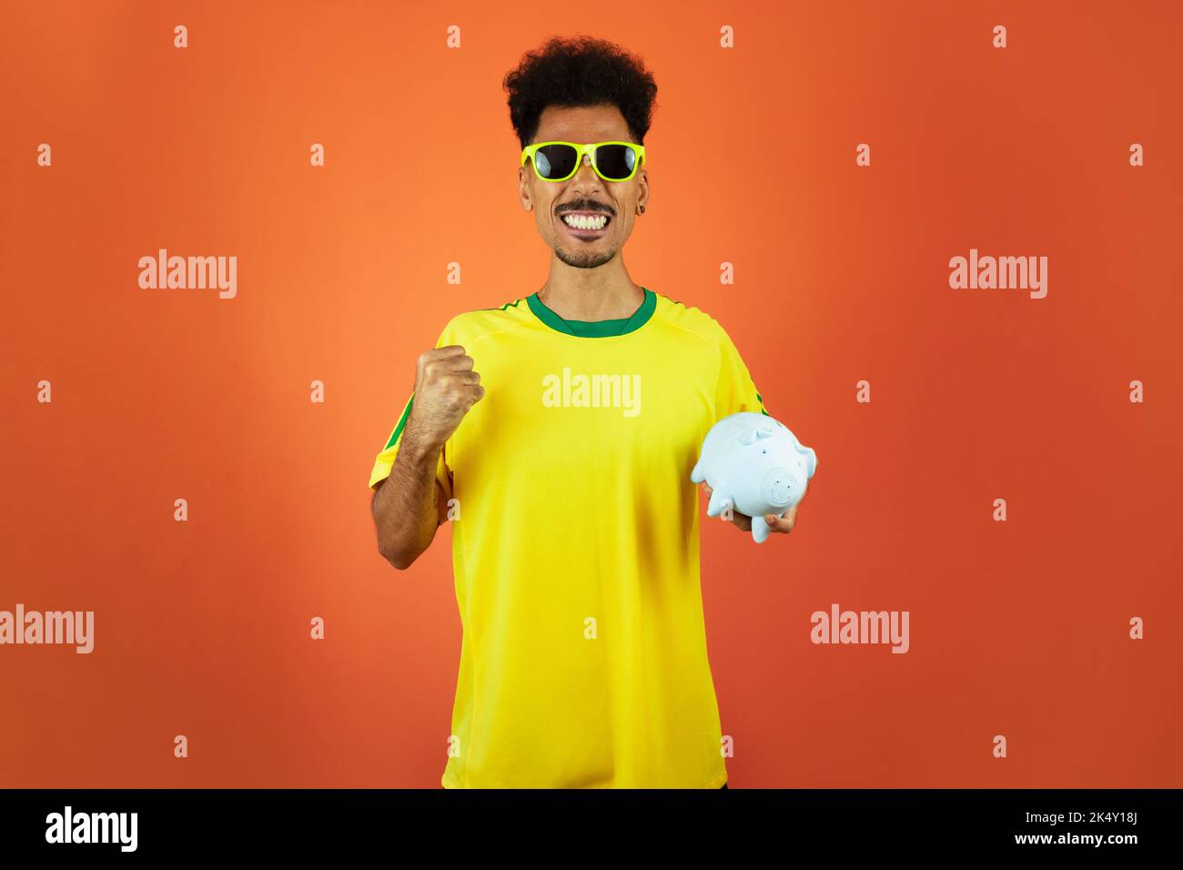 Fußballspieler - Schwarzer Mann feiert Holding Schwein Münze isoliert auf Orange Stockfoto