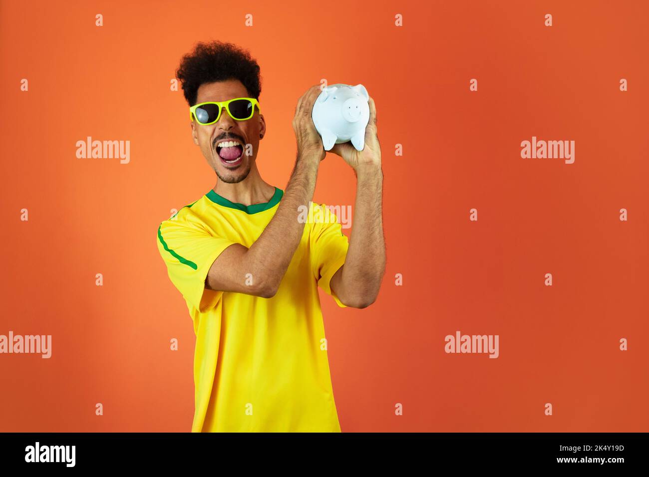 Fußballspieler - Schwarzer Mann feiert Holding Schwein Münze isoliert auf Orange Stockfoto