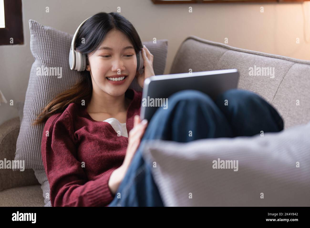 Attraktive lächelnde junge Frau mit Tablet und Musik hören auf dem Sofa zu Hause. Lifestyle-Konzept Stockfoto