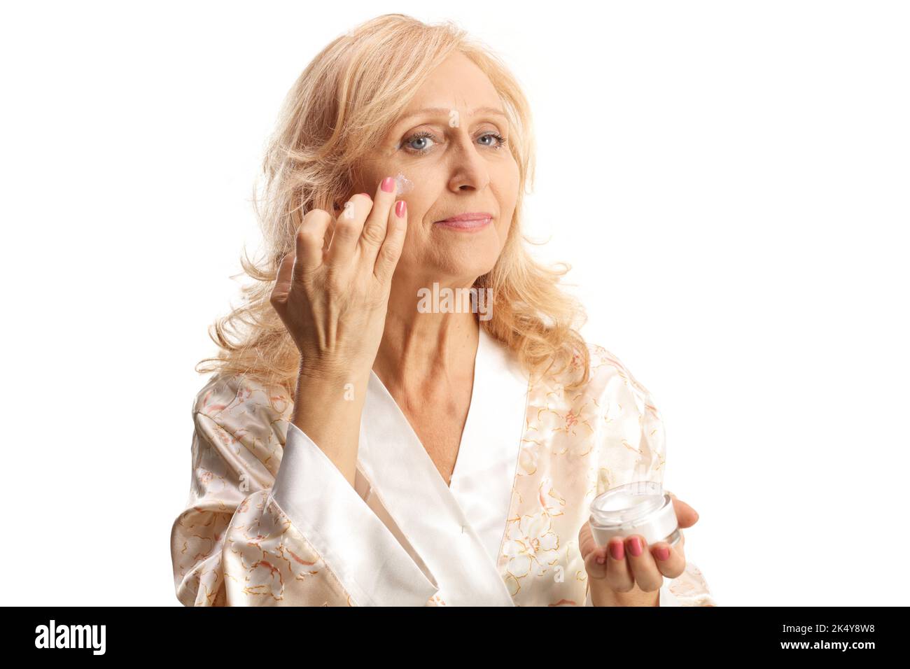 Schöne reife Frau in einem Bademantel Anwendung Anti-Aging Gesichtscreme isoliert auf weißem Hintergrund Stockfoto