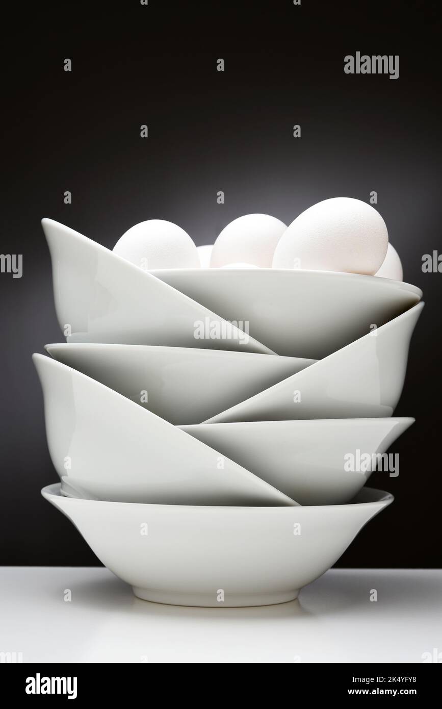 Stillleben. Eier in einer Gruppe von weißen, verschachtelten Schalen auf einem hellen bis dunklen Hintergrund. Stockfoto