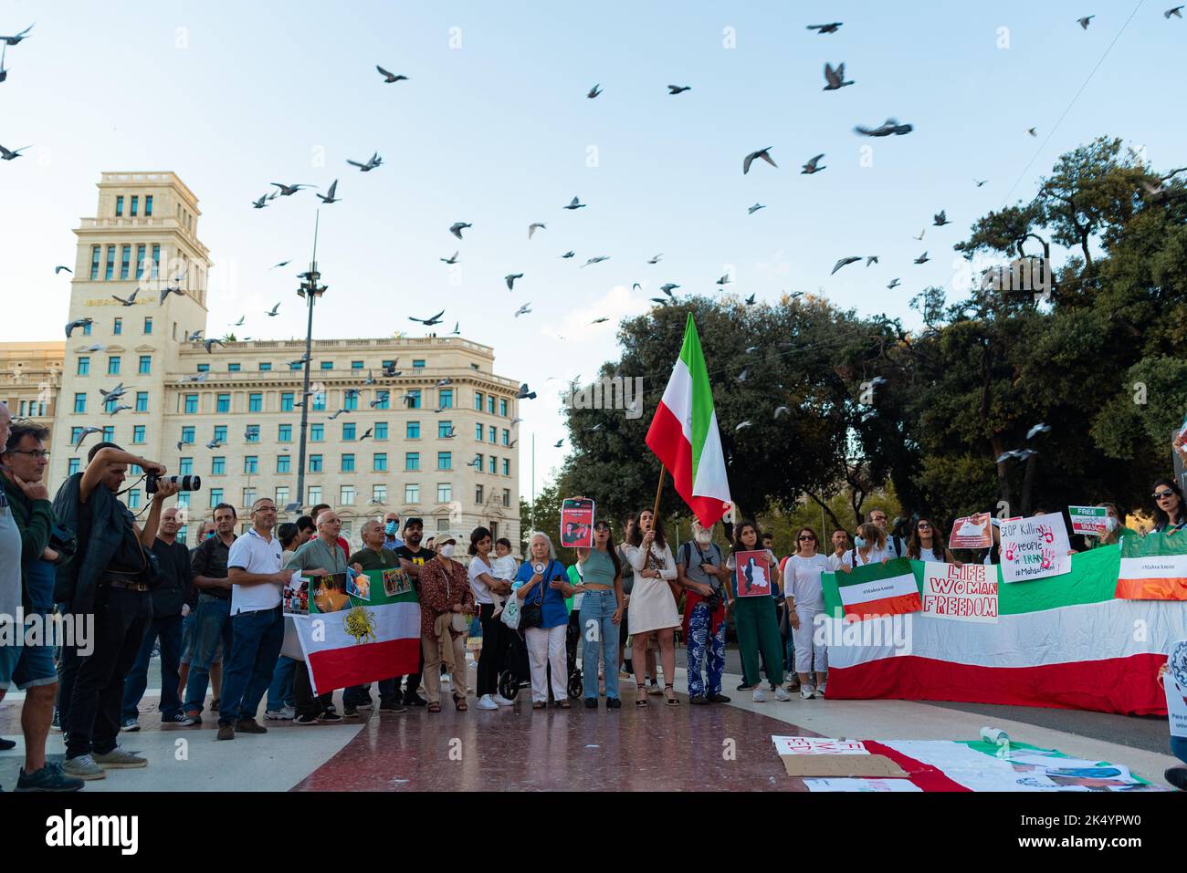 Barcelona, Spanien. 04. Oktober 2022. Vögel fliegen herüber, während Demonstranten Plakate und iranische Flaggen während der Demonstration halten. Ähnliche Demonstrationen wurden in Städten auf der ganzen Welt abgehalten, um Gerechtigkeit für die Tötung von Mahsa Amini zu fordern, einer jungen Frau, die von der iranischen Moralpolizei in Teheran inhaftiert wurde, weil sie den Hijab nicht ordnungsgemäß in der Öffentlichkeit trug. (Foto von Davide Bonaldo/SOPA Images/Sipa USA) Quelle: SIPA USA/Alamy Live News Stockfoto