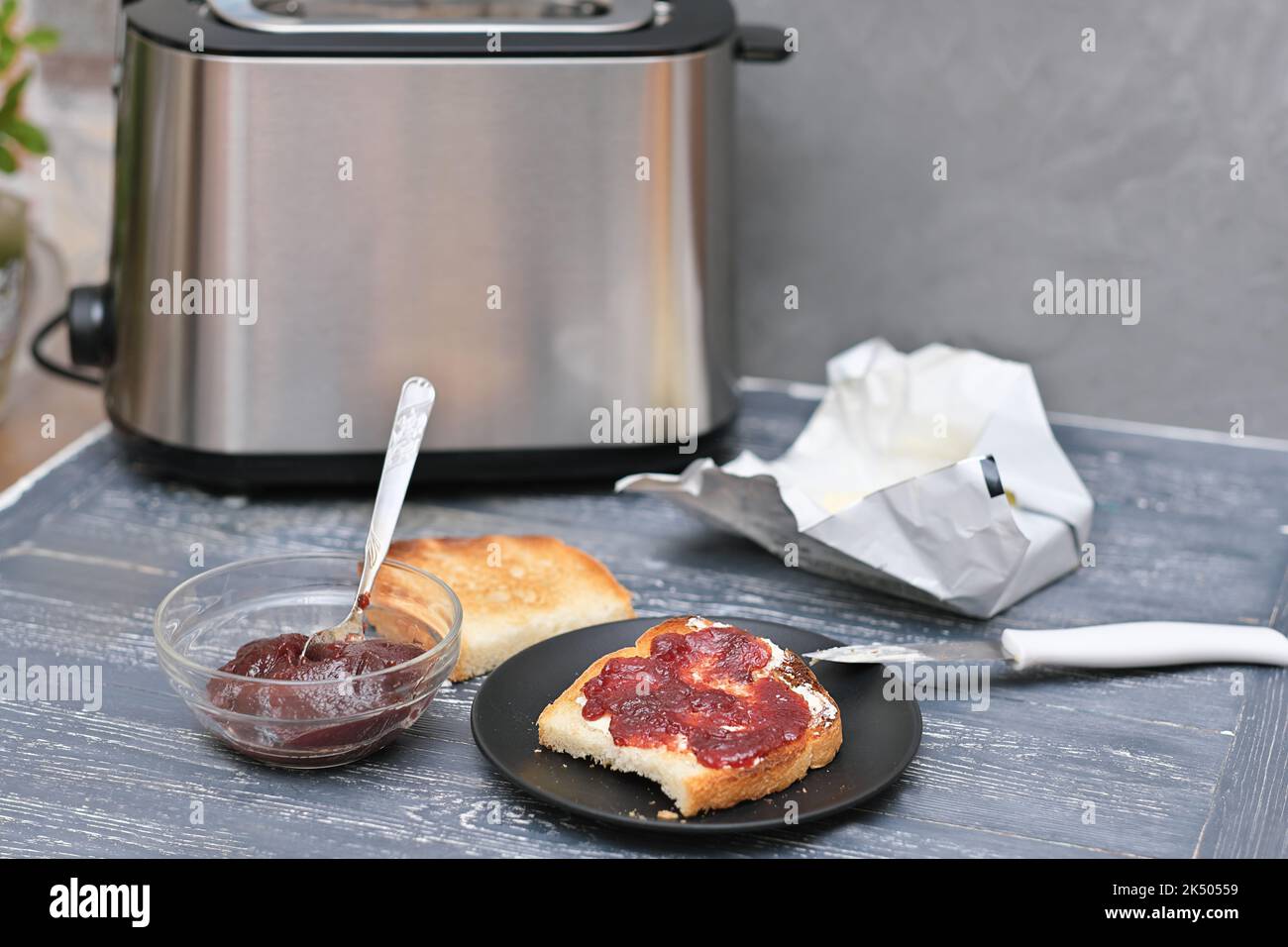 Toast mit Butter und Beerenmarmelade auf einem Holztisch neben dem Toaster. Frühstückszeit Stockfoto