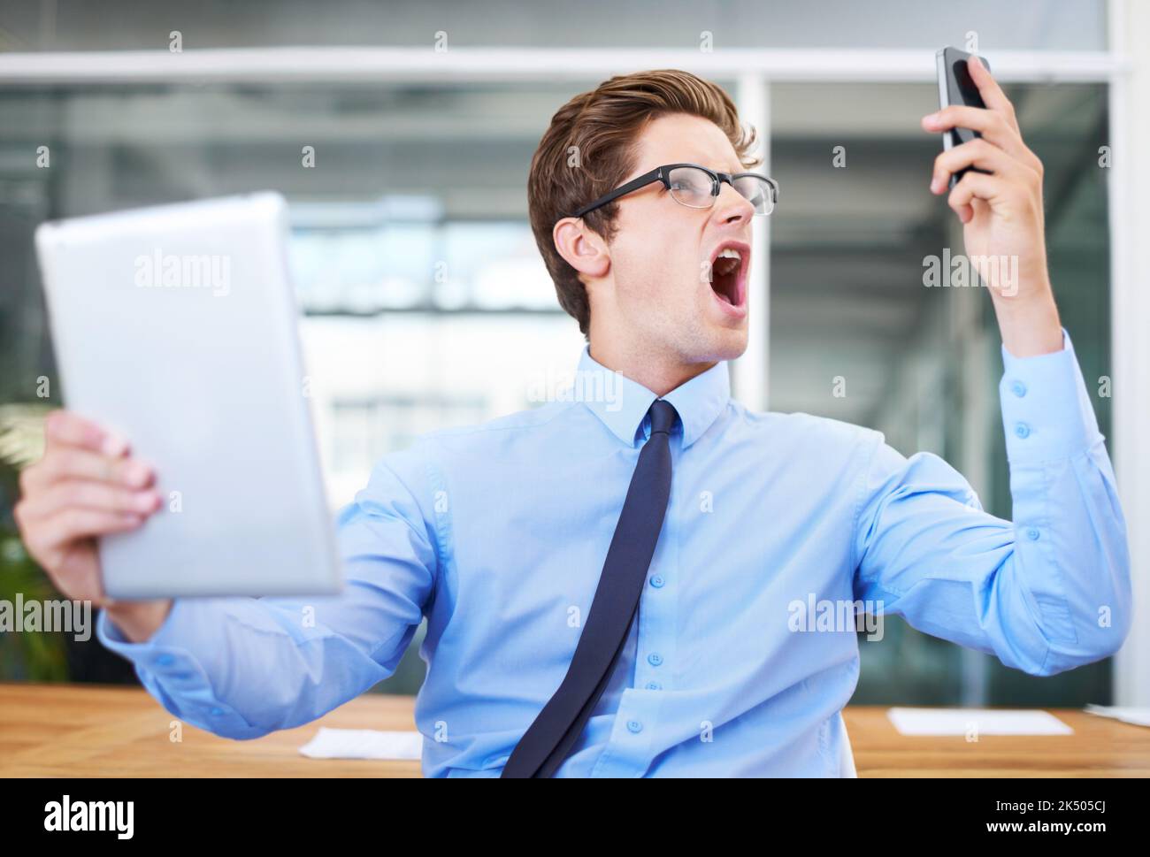 Das ist nicht hinnehmbar. Ein wütender junger Geschäftsmann schreit in sein Handy, während er ein digitales Tablet hält. Stockfoto