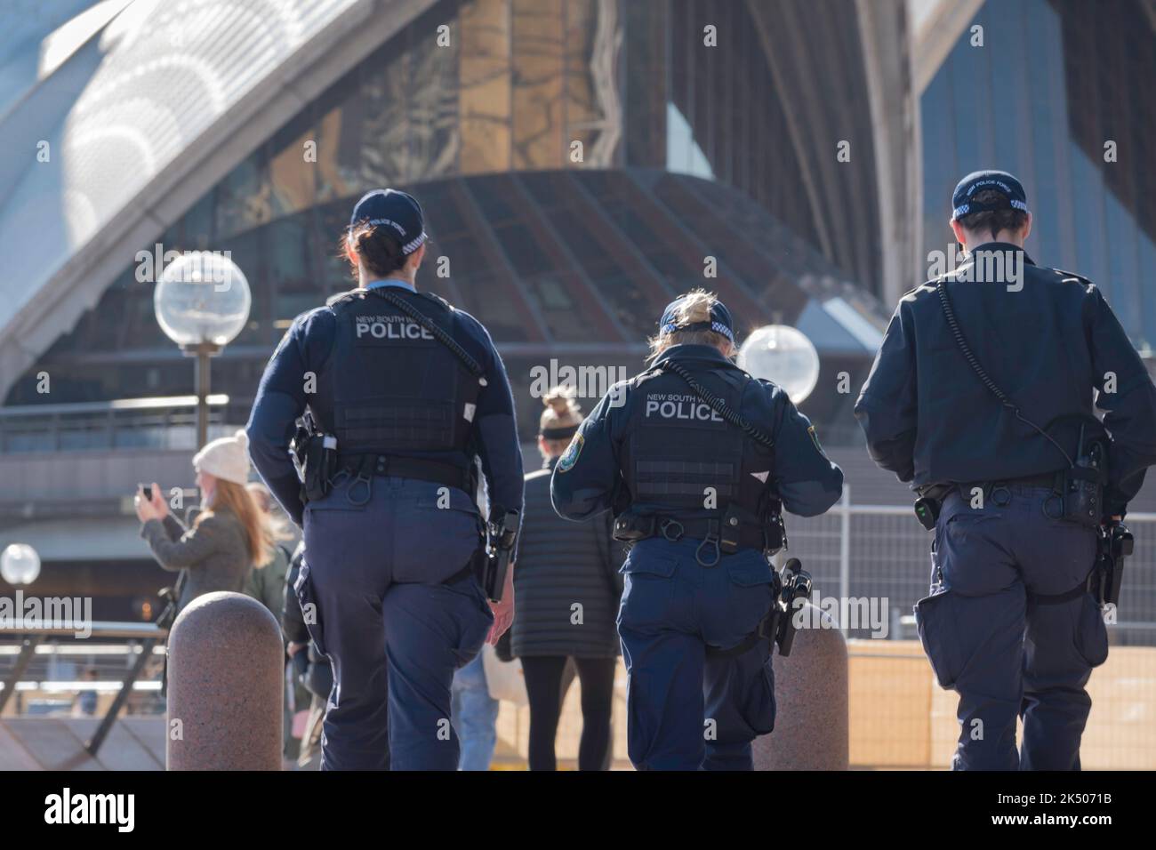 Drei Polizisten aus New South Wales, die morgens mit Seitenarmen auf einer Fußpatrouille unterwegs sind, laufen um den Vorplatz des Opernhauses von Sydney in Australien Stockfoto