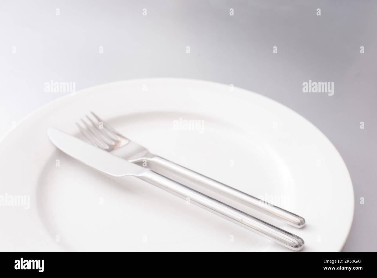 Leeren Sie saubere weiße Teller und Silberbesteck mit einem Messer und einer Gabel, die in der Mitte in einer beschnittenen Ansicht angeordnet sind Stockfoto