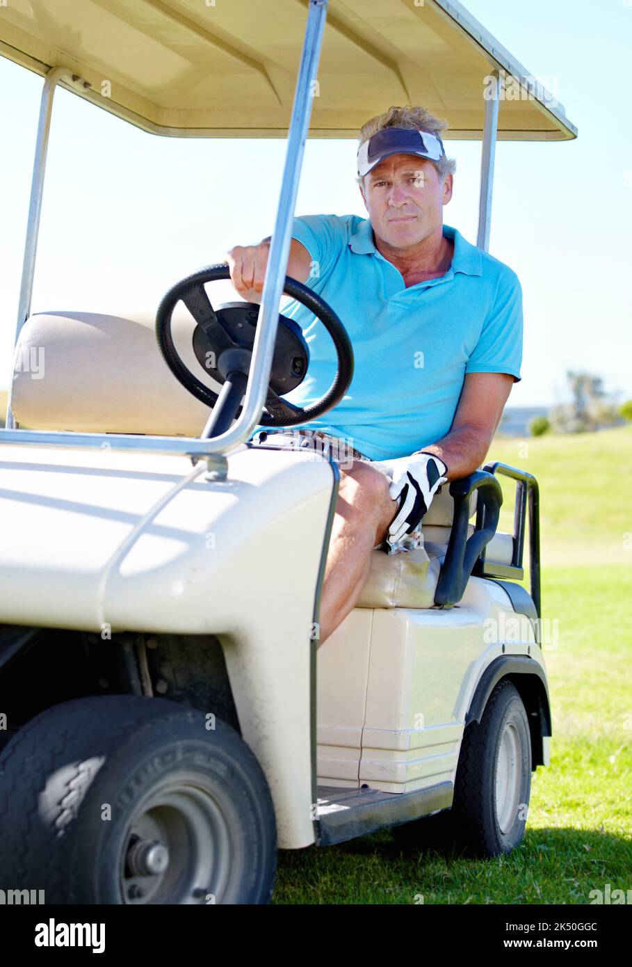 Auf dem Weg zum nächsten Loch. Ein reifer Mann, der einen Golfwagen über den Golfplatz fährt. Stockfoto