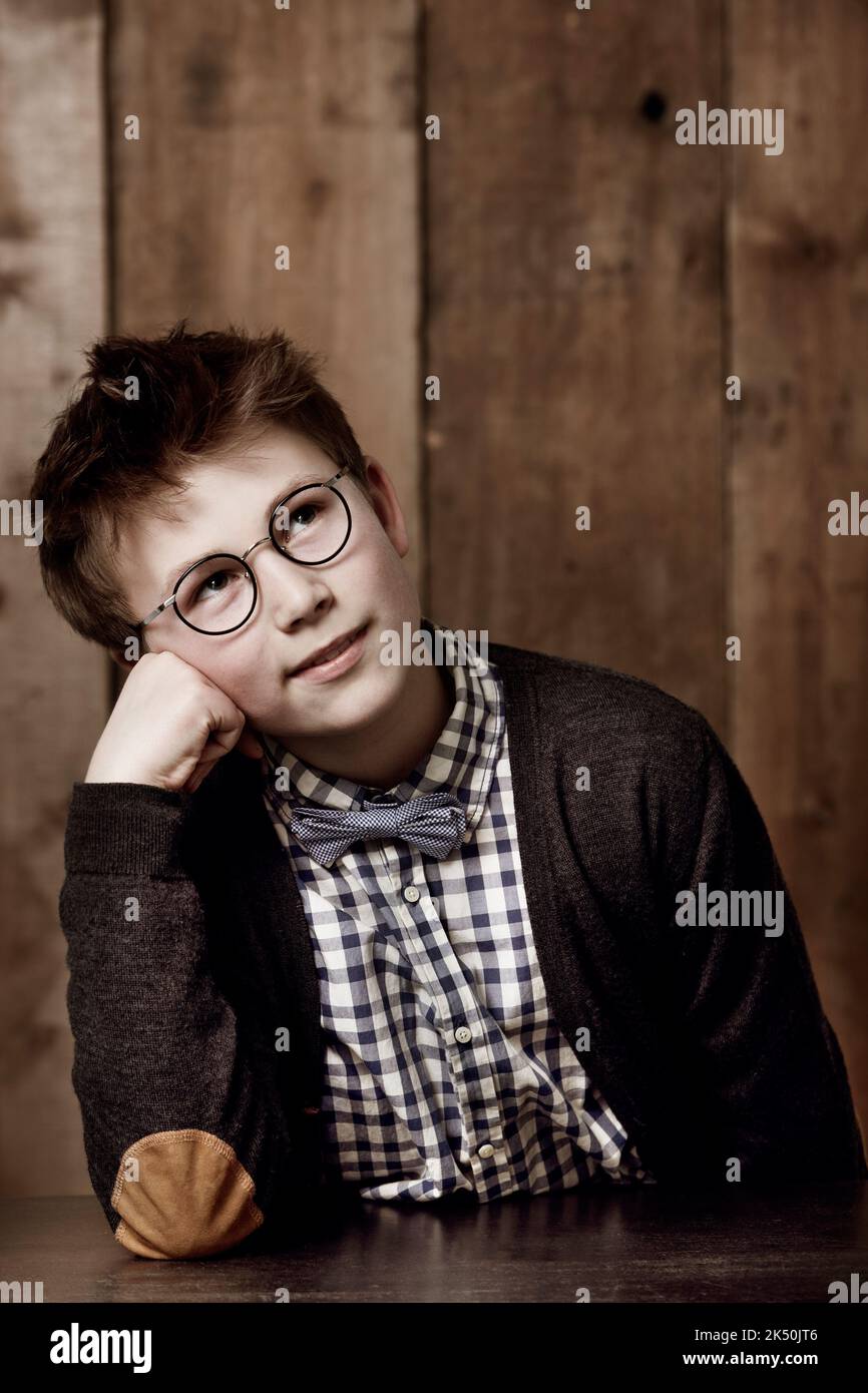 Tagträume von seiner Zukunft. Kleiner Junge in Retro-Kleidung, der eine Brille mit nachdenklicher Ausstrahlung trägt. Stockfoto