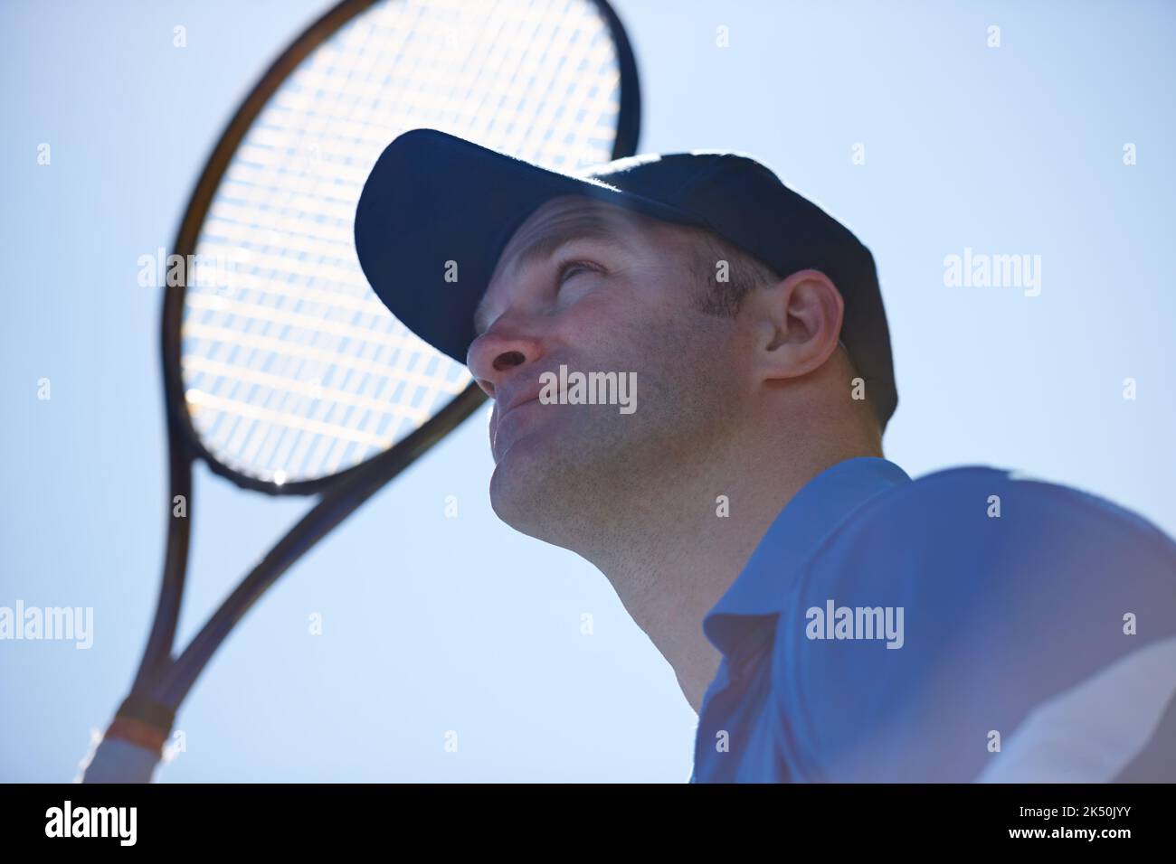 Tennis ist die pralle Sonne. Niedriger Blick auf einen männlichen Tennisspieler mit seinem Schläger, der vor einer prallen Sonne aufsteht. Stockfoto