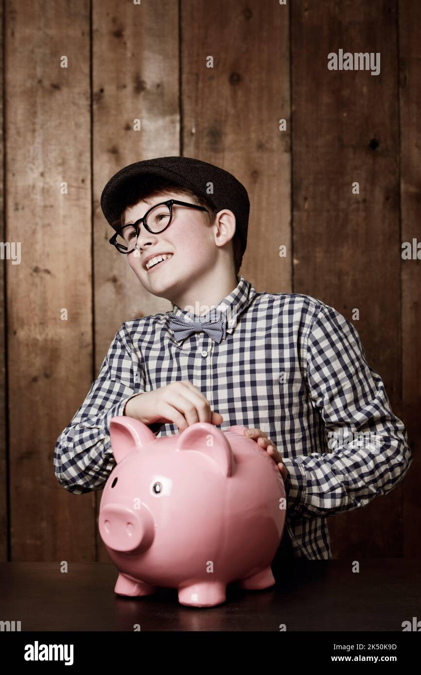 Jeden Cent sparen. Kleiner Junge in Retro-Kleidung, der Geld in sein Sparschwein gesteckt hat. Stockfoto