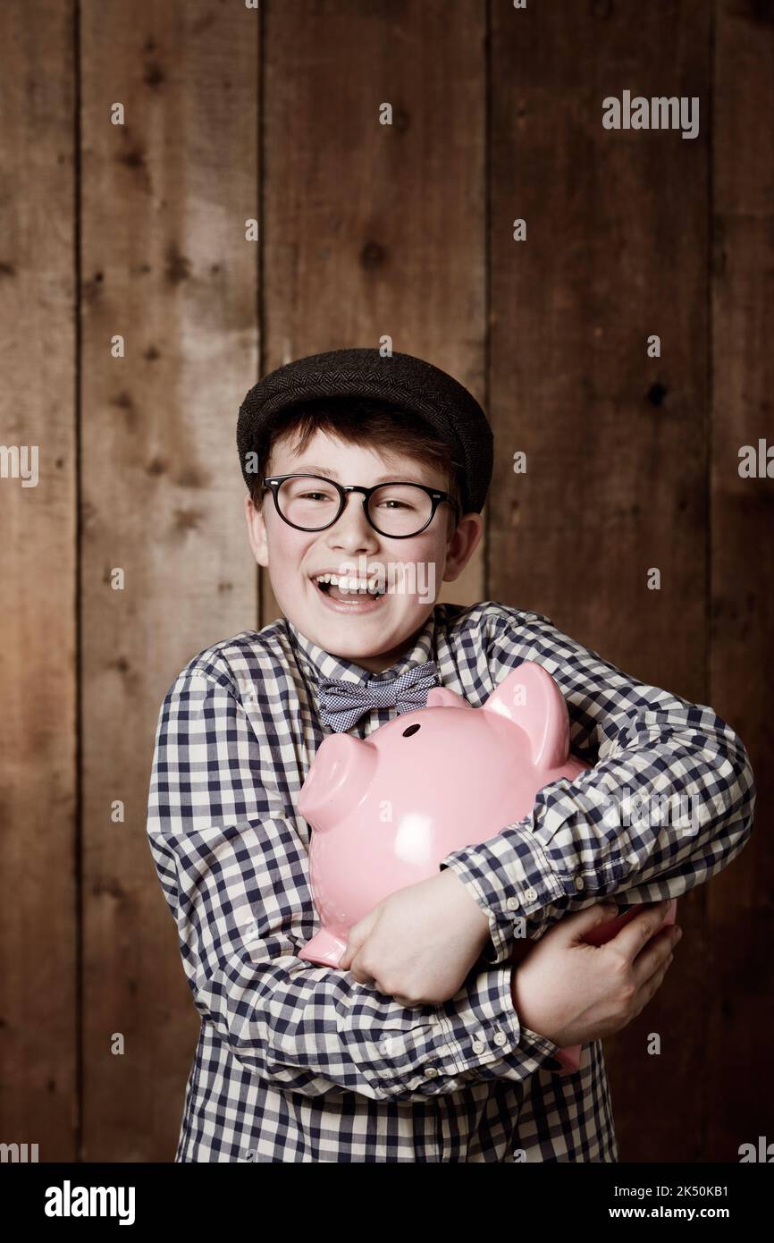 Ich liebe es zu sparen. Kleiner Junge in Retro-Kleidung, der sein Sparschwein fest umarmt. Stockfoto