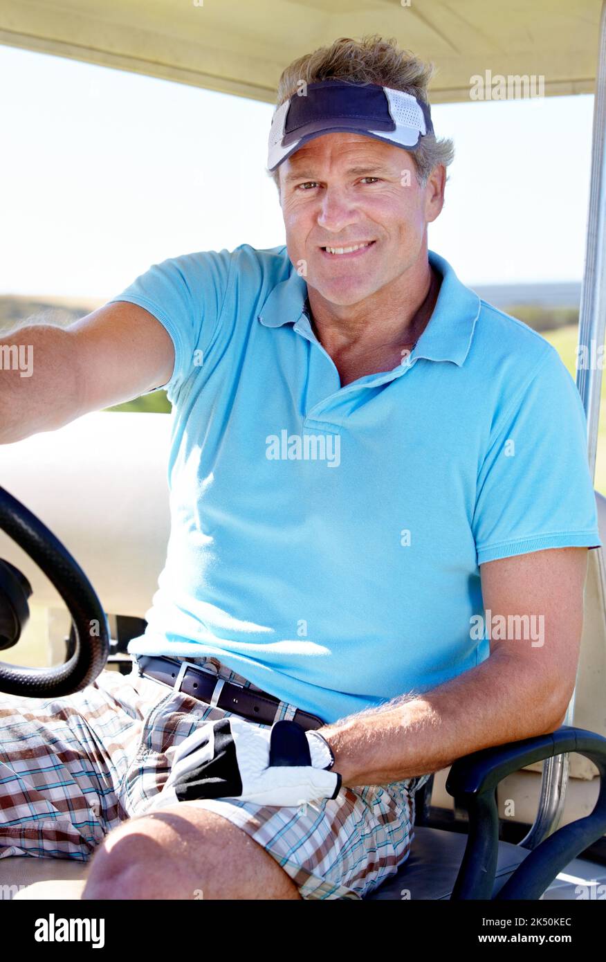 Golf ist mein Lieblingsort. Ein glücklicher reifer Mann lächelt, während er in einem Golfwagen sitzt. Stockfoto