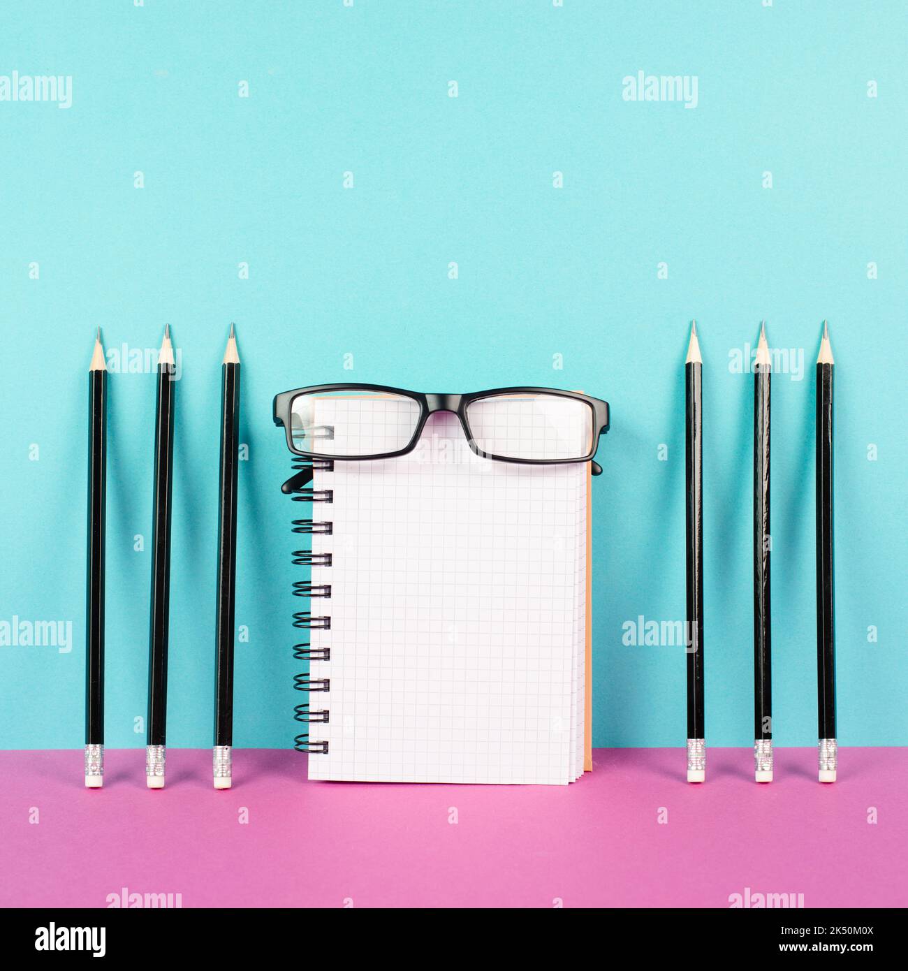 Leeres Notizbuch mit Bleistiften und Brillen auf rosa und blauem Hintergrund, Brainstorming für neue Ideen, Schreiben einer Nachricht, Schreibtisch im Home Office Stockfoto