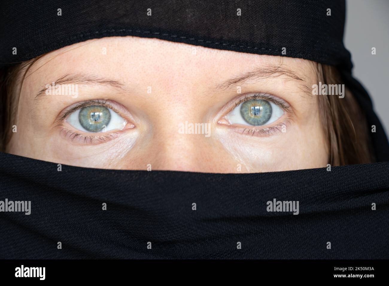 Das Mädchen bedeckte ihr Gesicht und ihren Kopf mit einem schwarzen Schal auf einem isolierten Hintergrund, der Glaube und die Religion sind muslimisch Stockfoto