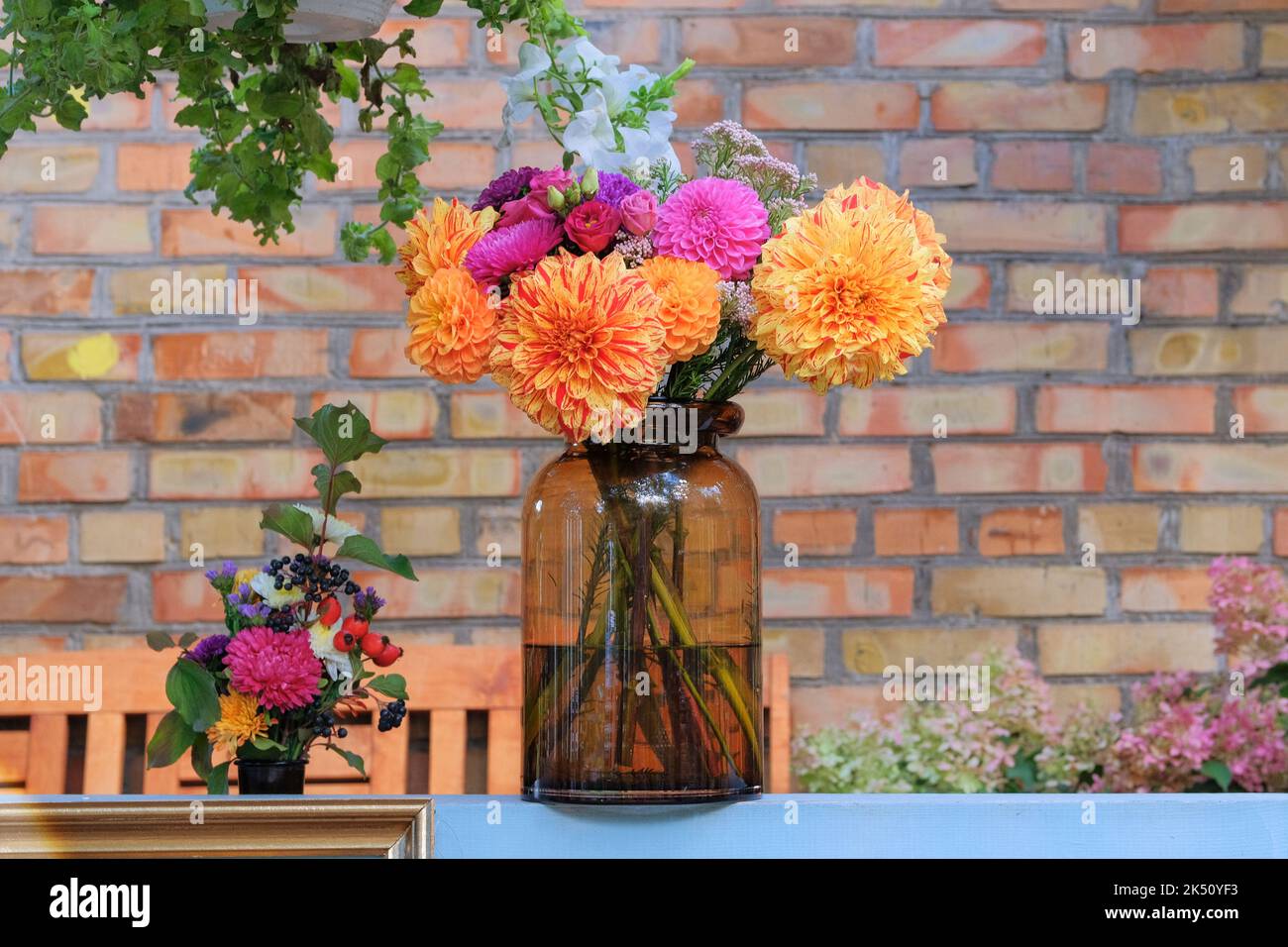 Rosen, Aster, Dahilia in Glasvase im Garten auf dem Hintergrund einer Ziegelmauer. Sonniger Tag. Floristisches Design. Stockfoto